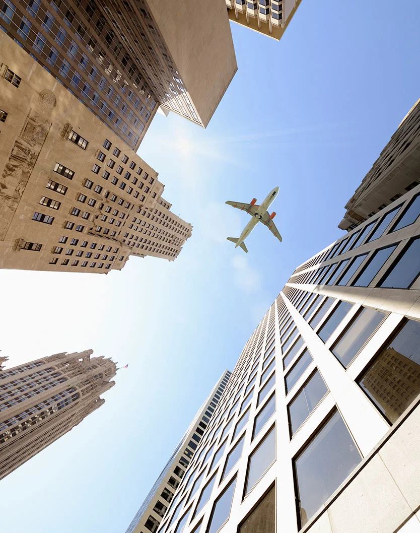 upward view of a plane over skyscrapers in Chicago -Plastic Surgery Out of Town Patient Resources in Chicago, IL